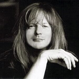 Black and white portrait of American Christian rock musician Larry Norman, looking directly forward with long blonde hair.